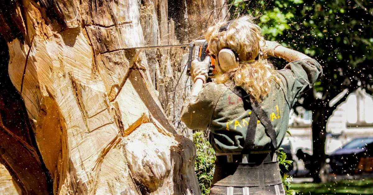 Une femme arboriste qualifiée coupe un grand arbre avec une tronçonneuse en extérieur, montrant son expertise en soins arboricoles.