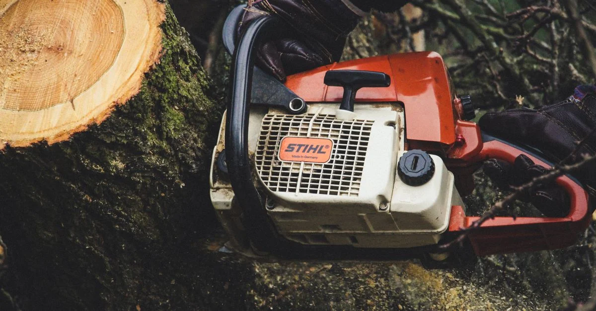 Une personne utilise une tronçonneuse pour couper un tronc d'arbre en plein air, mettant en avant les travaux forestiers.