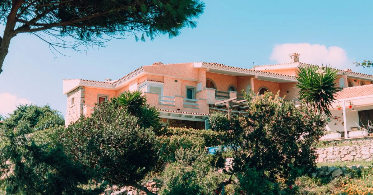 Charmante villa méditerranéenne nichée dans des jardins vibrants et luxuriants sous un ciel bleu clair.